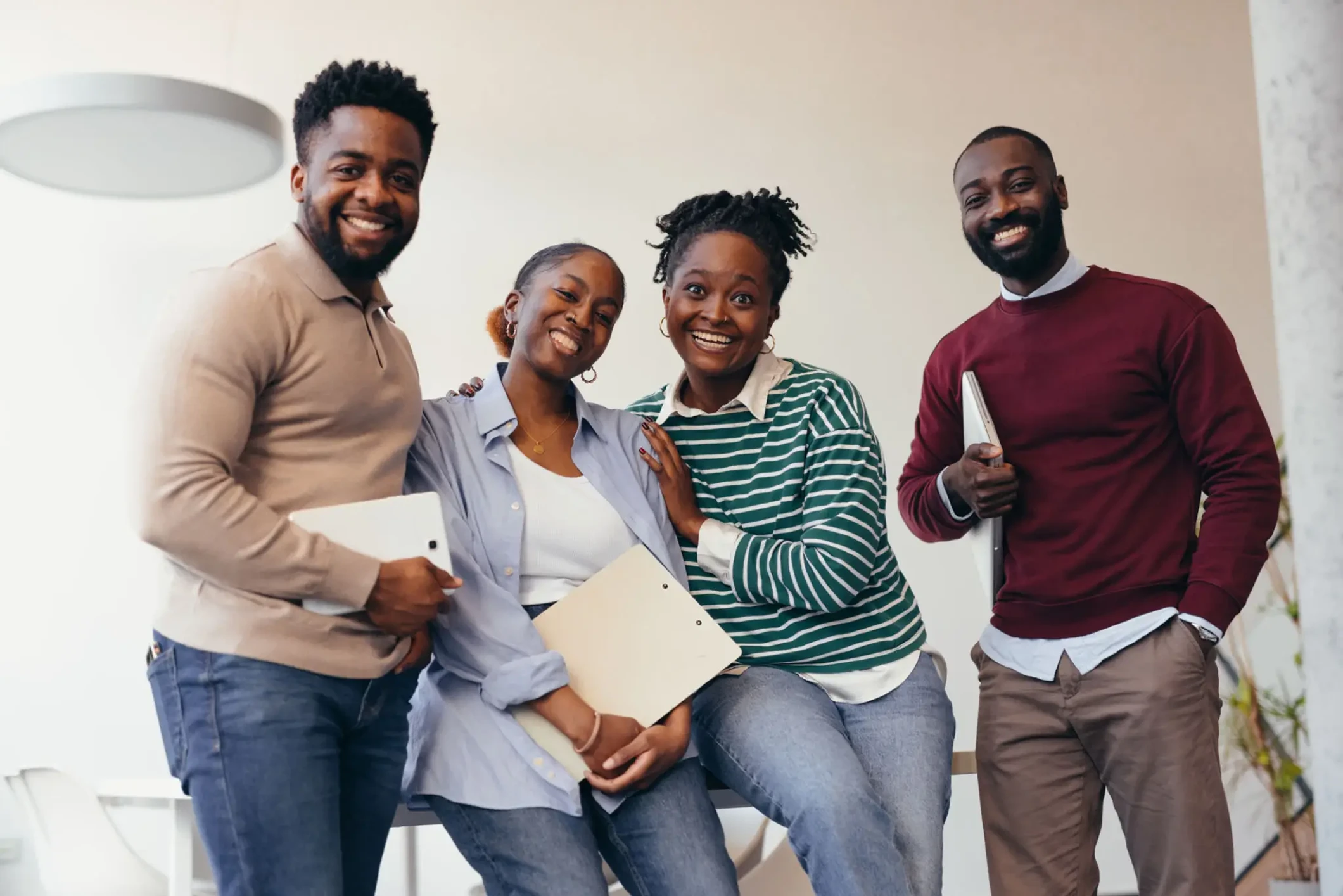 Four people smiling, holding notebooks, indoors.