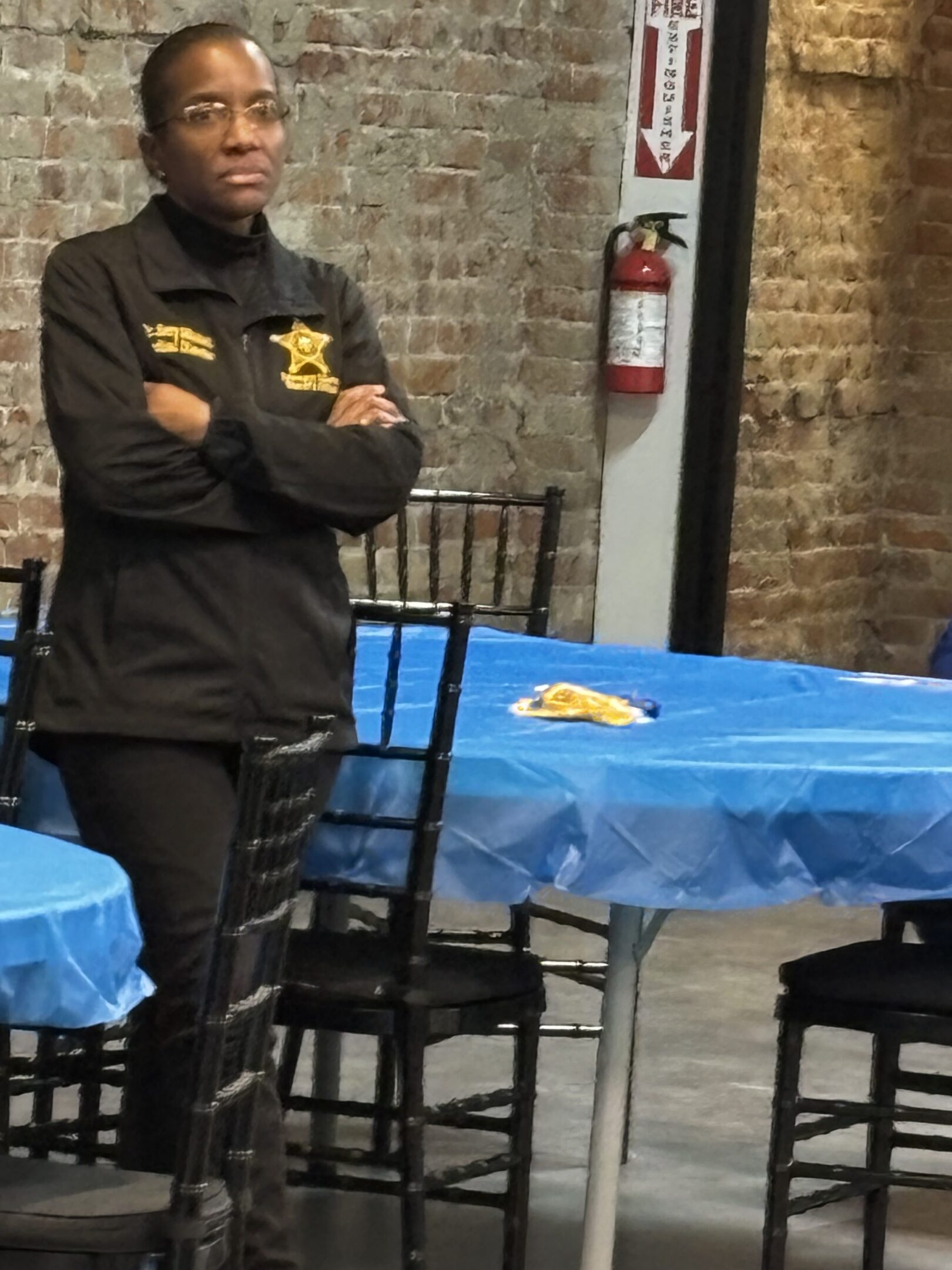 Man in black chef coat with gold embroidery standing with arms crossed.