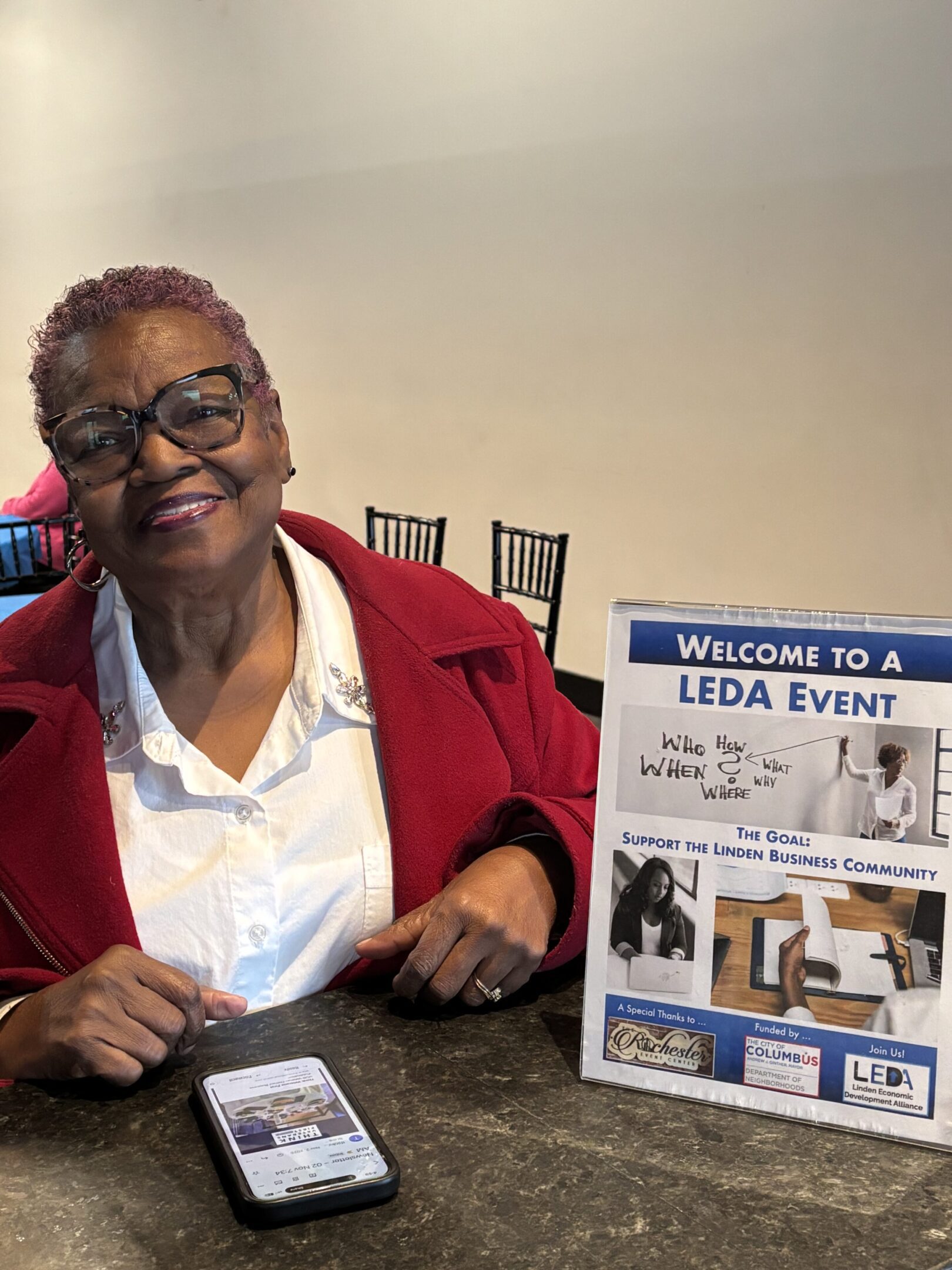 Elderly woman smiling at a LEDA event table with informational materials.