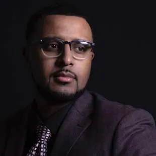 Portrait of a man wearing glasses and a suit against a dark background.
