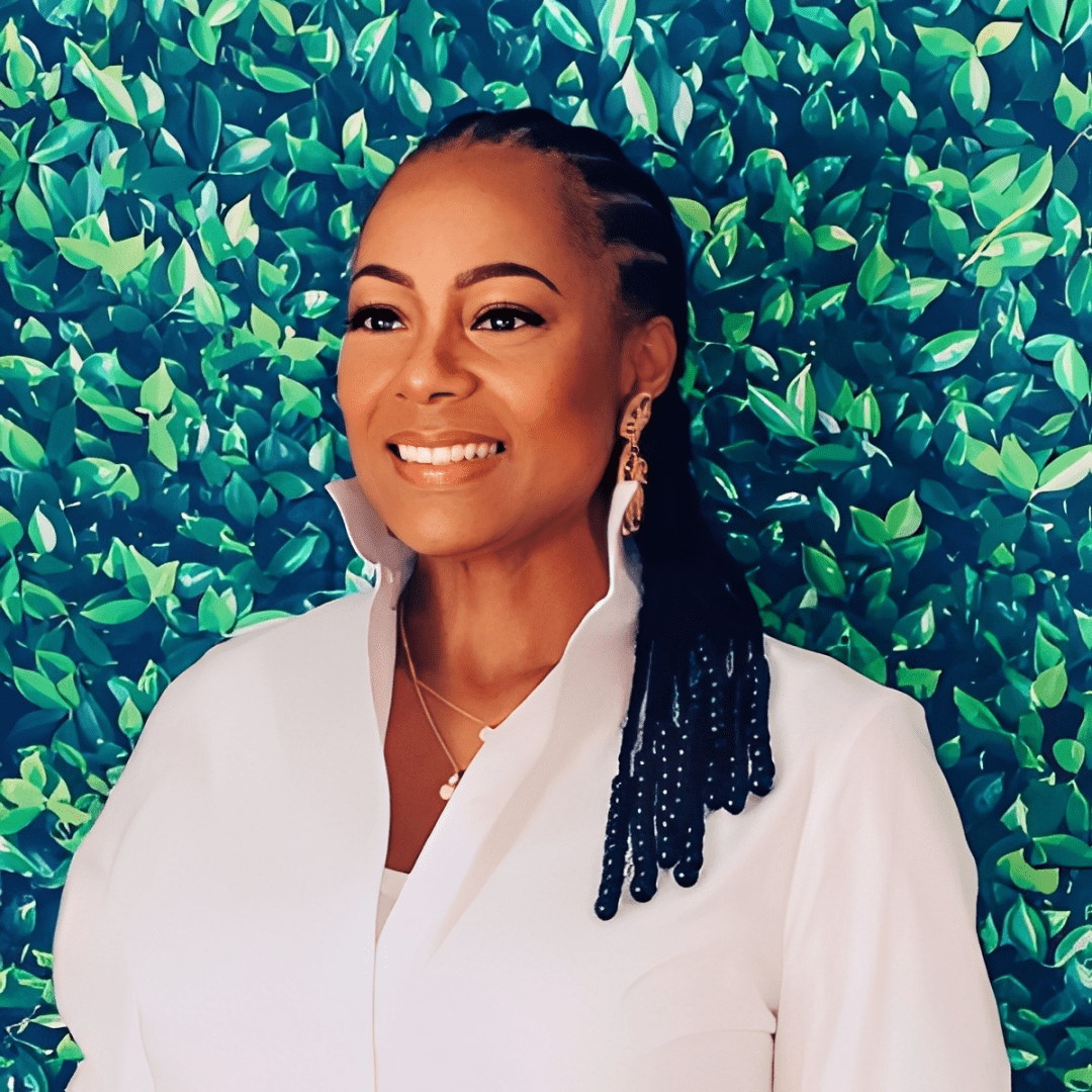 Smiling woman with braided hair stands before a vibrant green leafy backdrop.