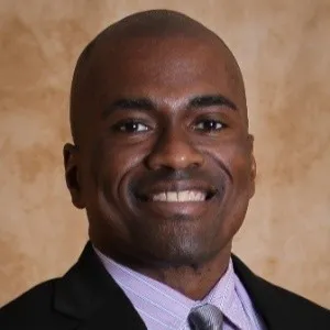 A smiling man in a suit and tie against a neutral background.