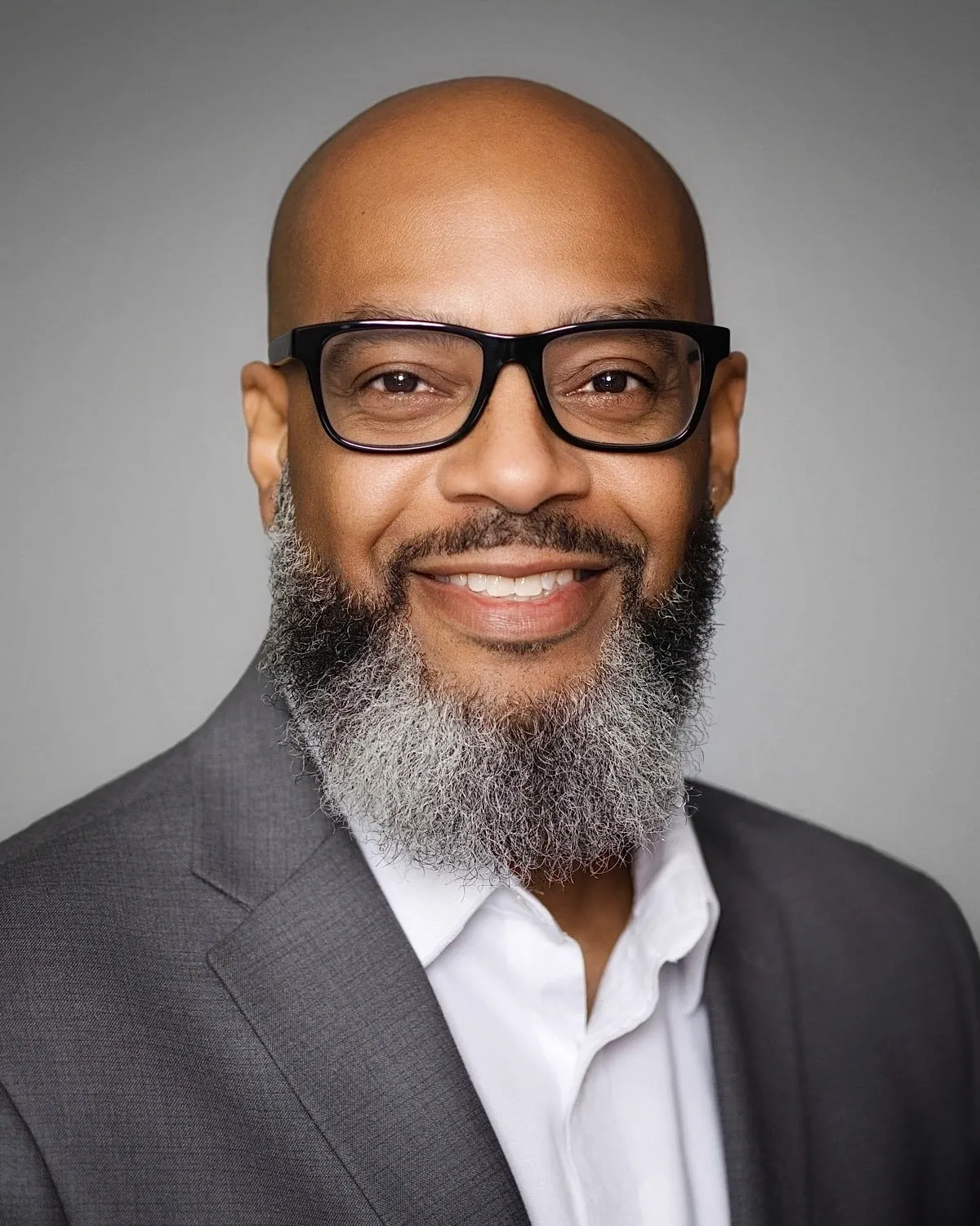 Smiling man with a beard and glasses in a suit.