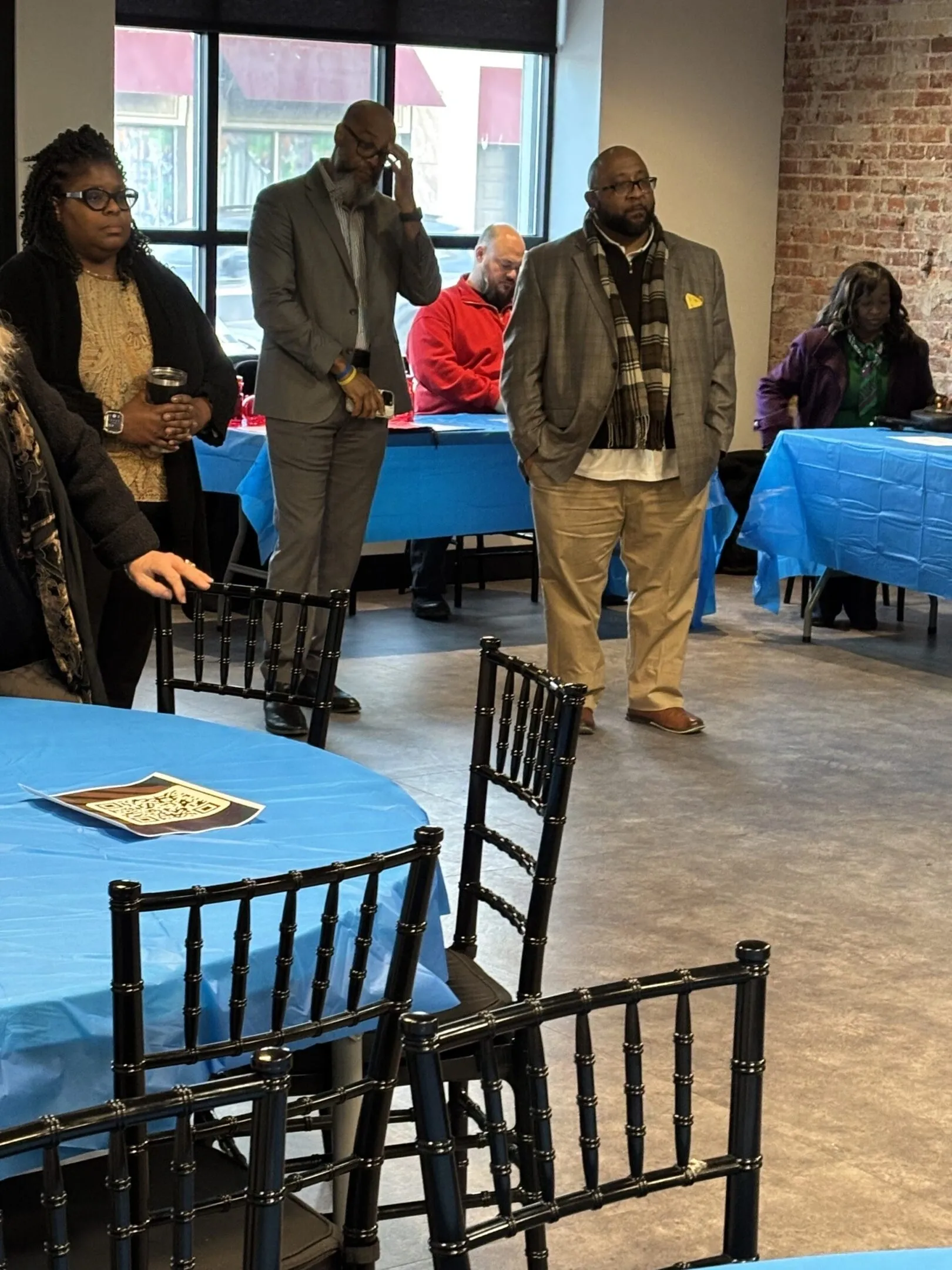 People engaging in a casual indoor gathering with blue tablecloths and black chairs.