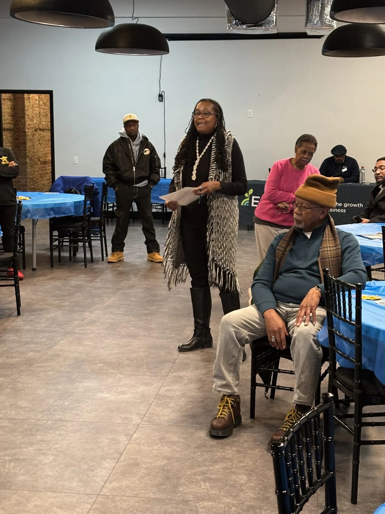 A woman speaks to an audience in a casual indoor event.