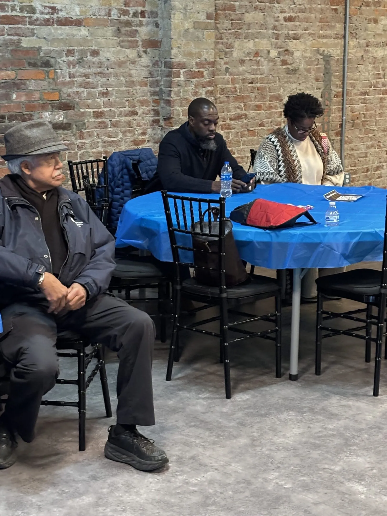 Three men sitting at a table with a blue tablecloth in a casual setting.