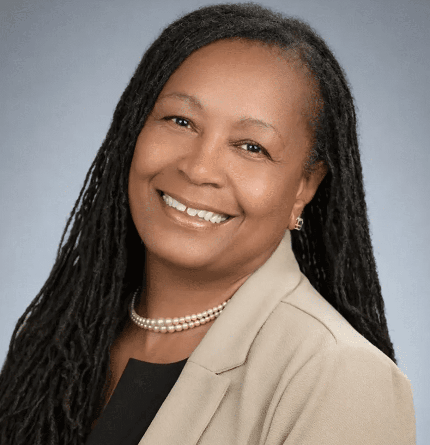 Professional woman with long braided hair smiles warmly in a business portrait.