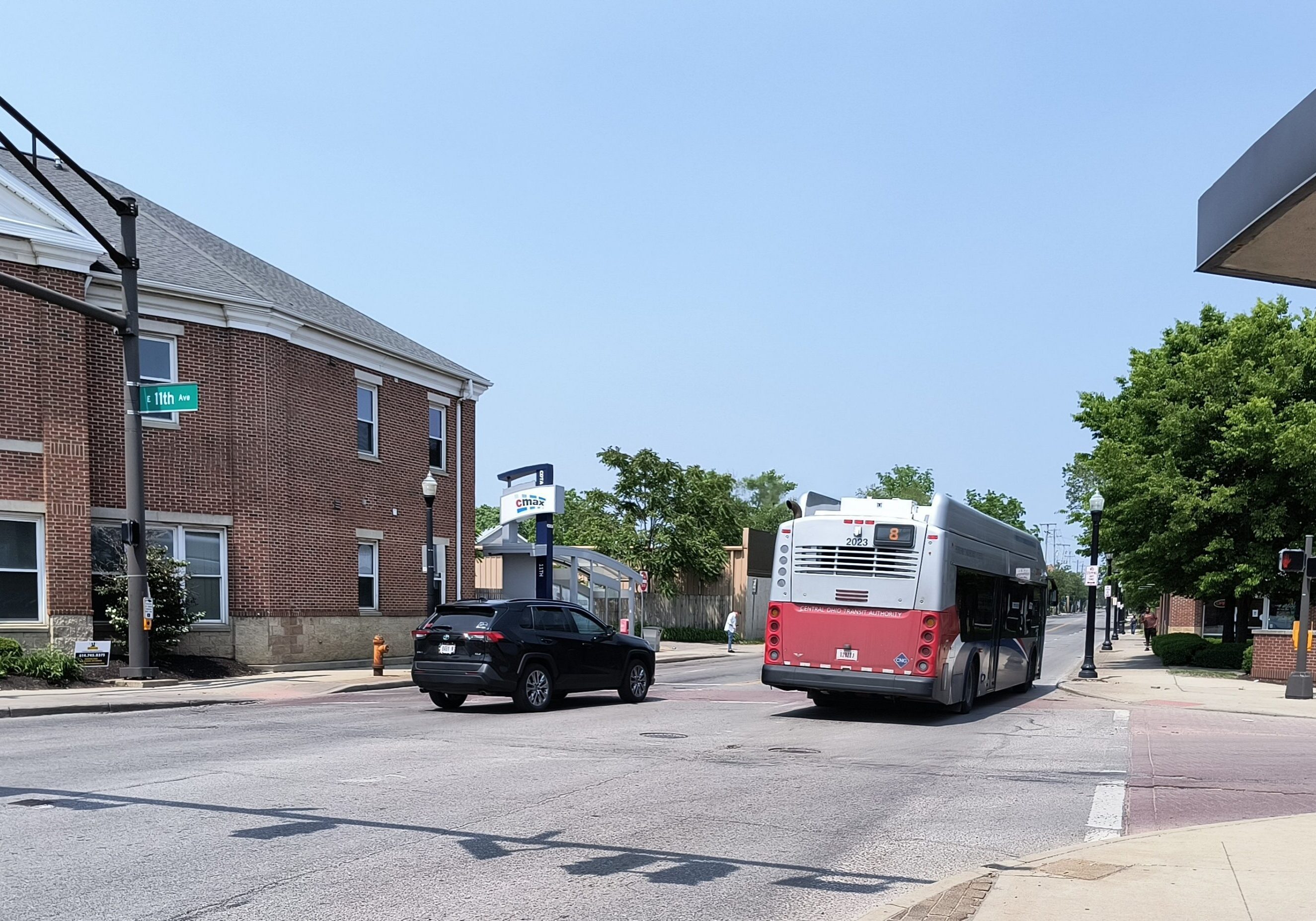 A city bus and a black SUV on a street near a brick building under clear sky.